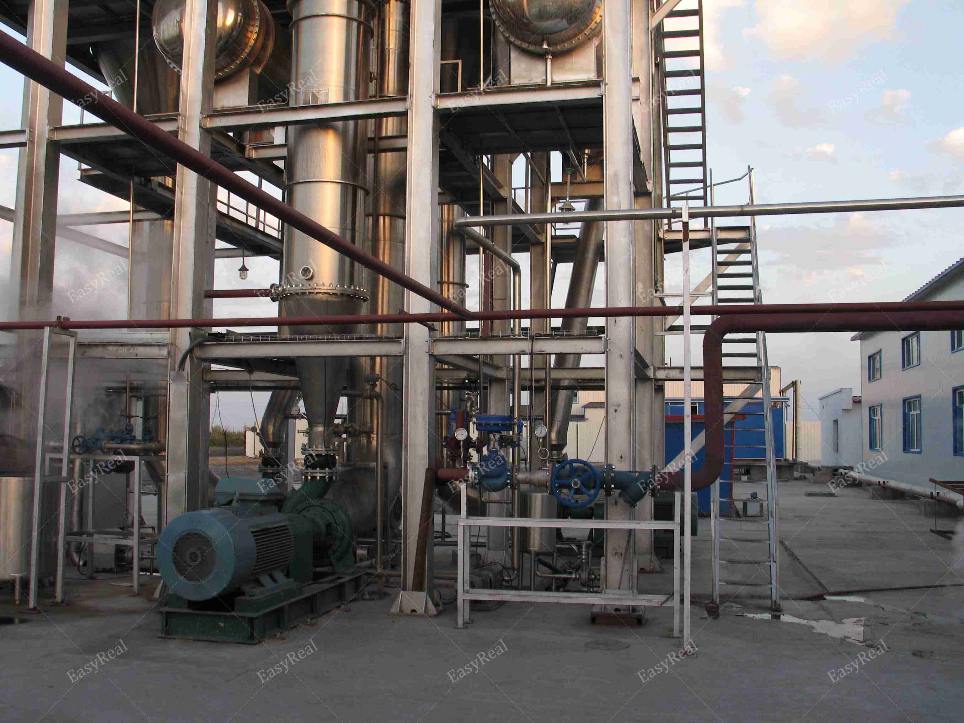 Close-up of the bottom part of a forced circulation evaporator showing steam pipes, large recirculation pump and structural frame in an outdoor tomato paste concentration plant.