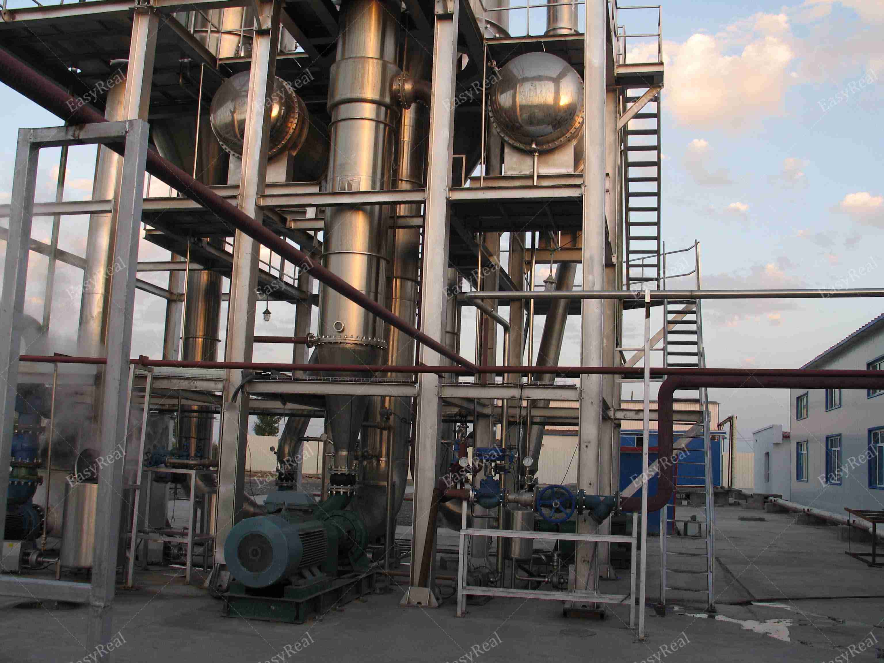 Front view of EasyReal multi-effect forced circulation evaporator showing vertical columns, spherical separator vessels, platforms and access ladder in a tomato paste concentration plant.