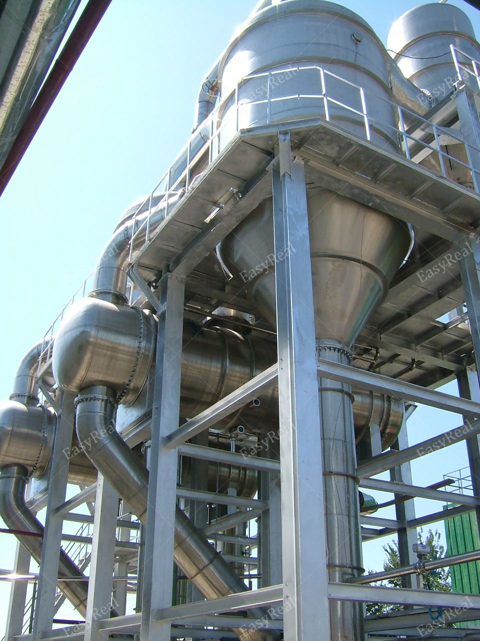 Upward view of the top section of a forced circulation evaporator tower with circular separators, platforms and railings, installed in an industrial tomato paste and fruit puree factory.