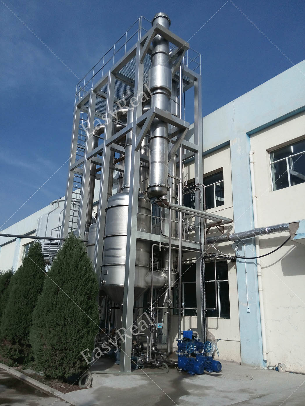 Outdoor installation of EasyReal multi-effect falling film evaporator tower with access platform beside the processing workshop for fruit and tomato juice concentration.