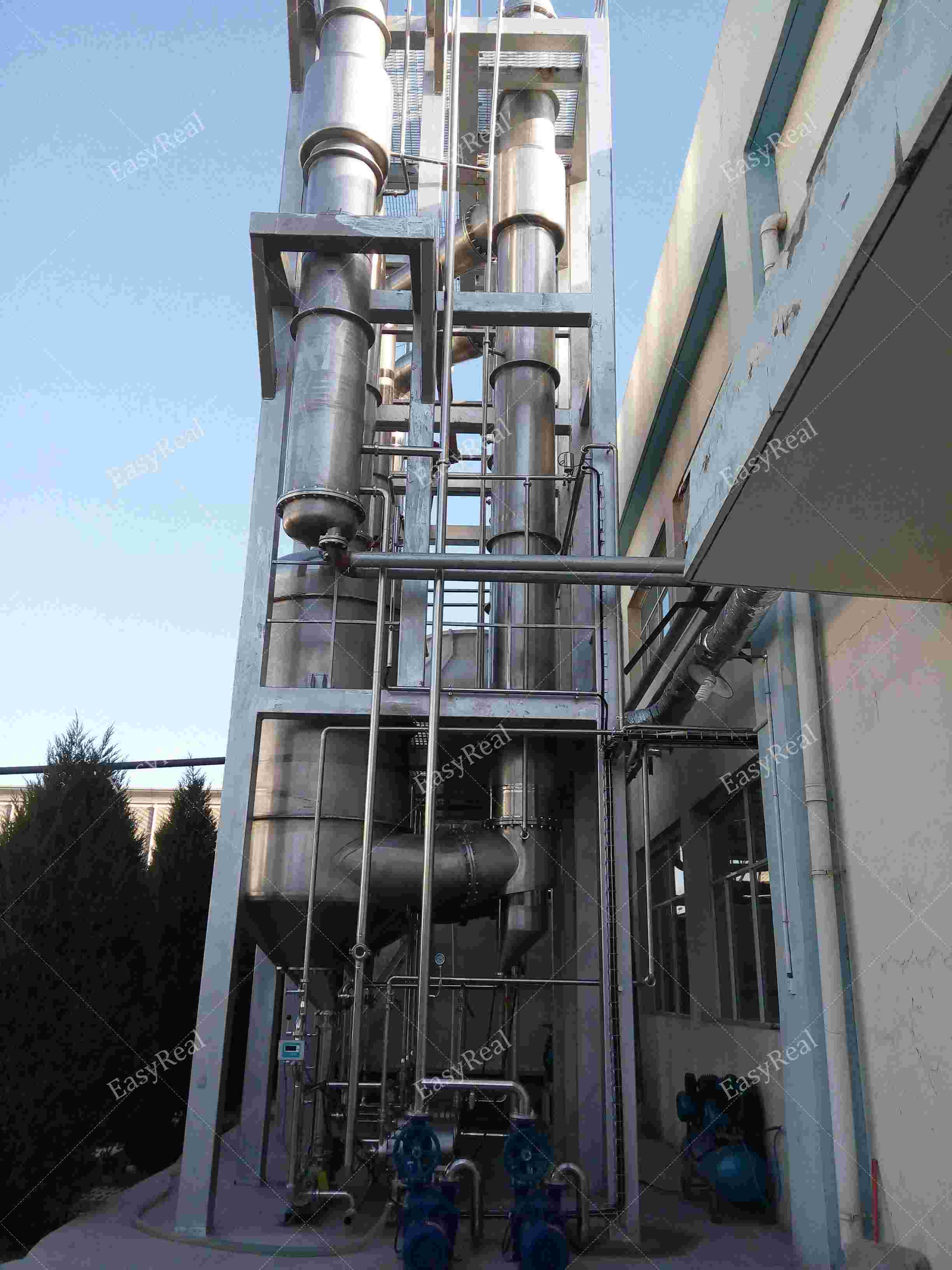 Outdoor stainless steel multi-effect falling film evaporator tower with vertical columns, platforms, piping and feed pumps installed beside EasyReal fruit and vegetable juice concentration plant.