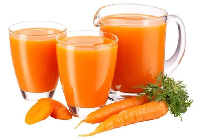 Glasses and jug filled with bright orange carrot juice with fresh carrots beside, representing juice products from an industrial carrot juice processing line.