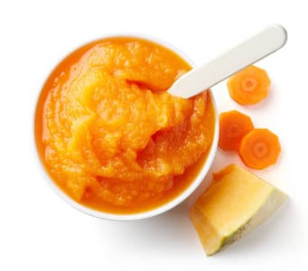 Bowl of smooth orange carrot puree with spoon and carrot slices, typical end product of an industrial carrot puree processing line for baby food and vegetable sauces.