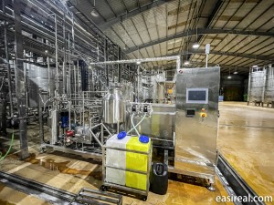 On-site view of a tubular UHT sterilizer skid supplied and installed by Shanghai EasyReal at the FGC beverage factory in Vietnam. The stainless-steel system includes the main sterilization unit, PLC touch-screen control cabinet, and chemical dosing tanks, surrounded by process pipelines and storage tanks inside the production workshop.