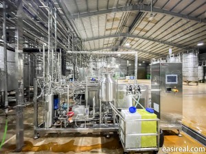 Front view of a tubular UHT sterilizer skid supplied and installed by Shanghai EasyReal at the FGC beverage factory in Vietnam, showing the main sterilization unit, holding tank, CIP chemical trolley, and surrounding stainless-steel pipelines inside the production workshop.